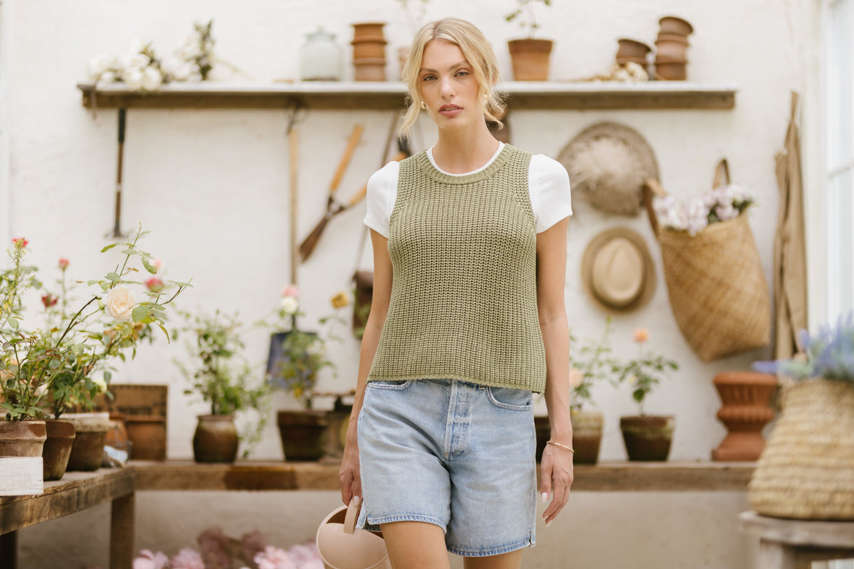 A woman walking in the Gentle Fawn knit vest paired with blue denim shorts.