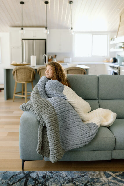 Woman sitting on couch with Nicole's cozy knit blanket, available at Lemonberry.