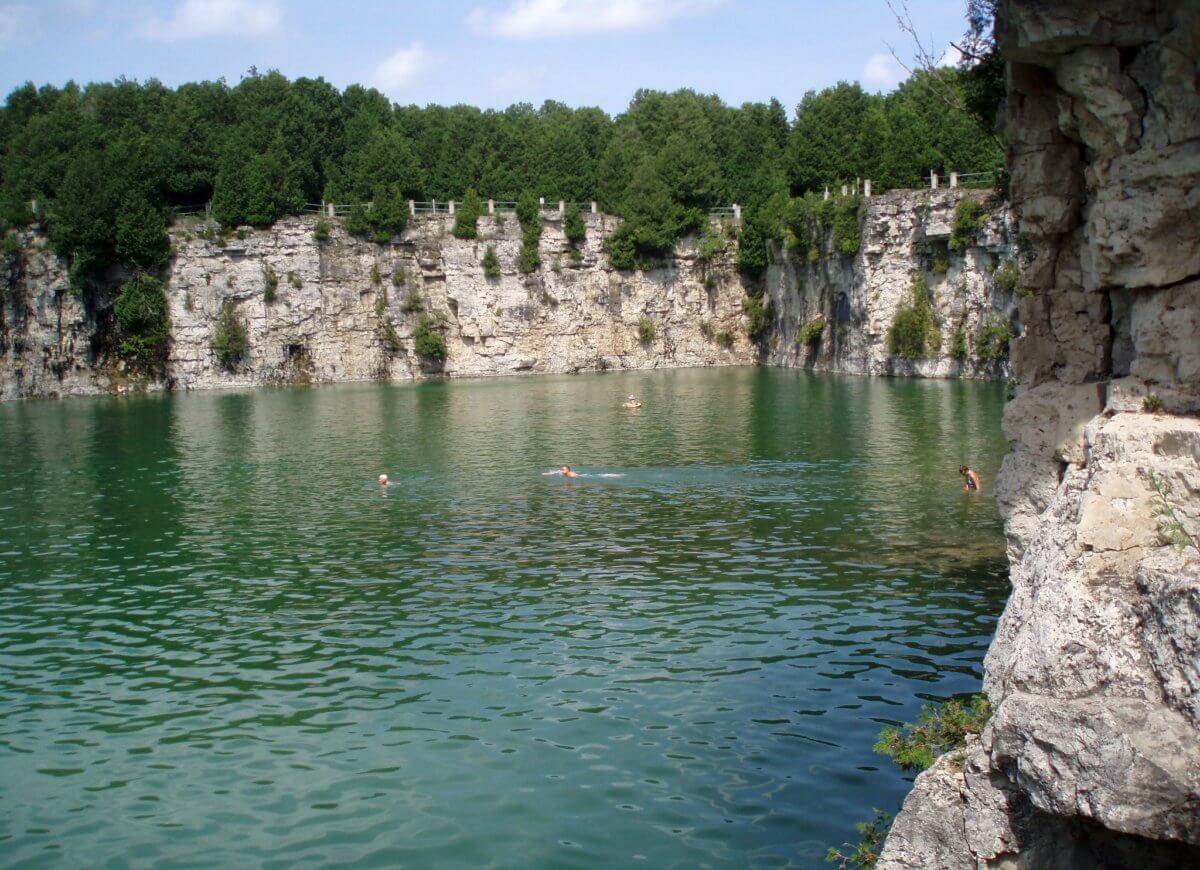 Swimmers floating in a turquoise quarry surrounded by limestone cliffs and cedar trees in Elora