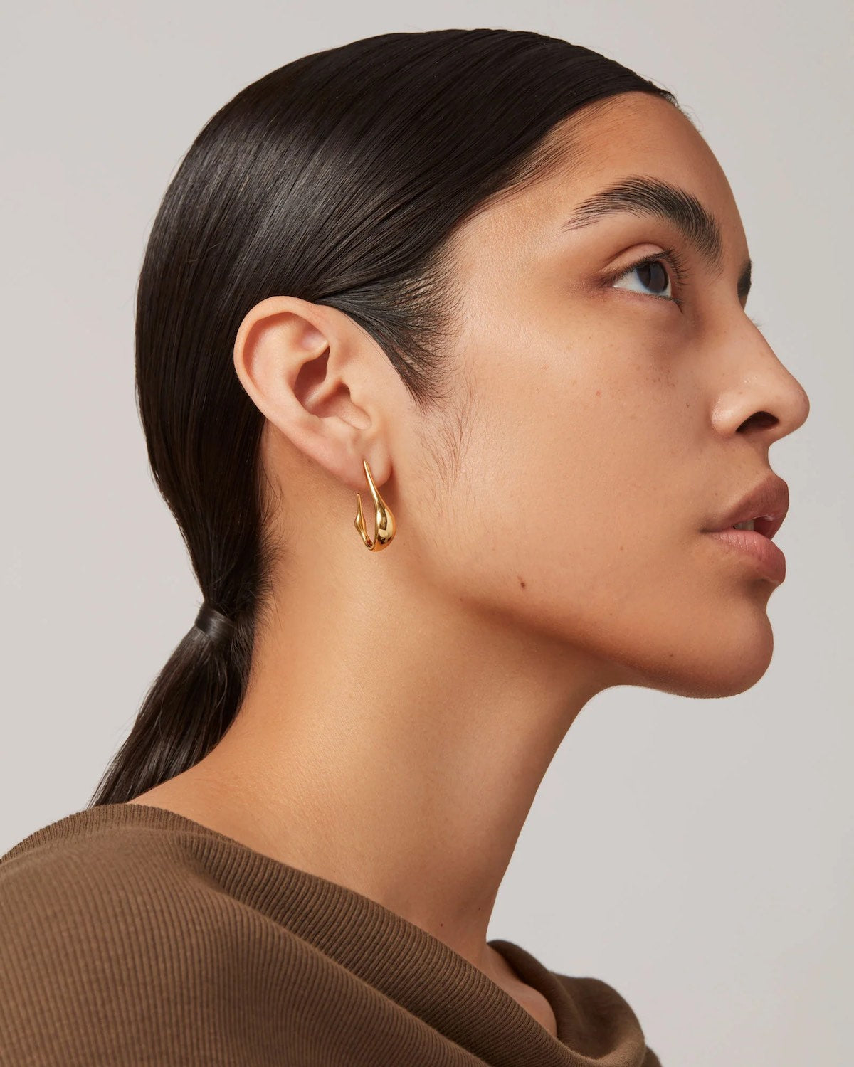 Woman wearing Colette gold hoop earrings with a neutral background