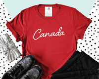 A flat lay of our Canada Tee in red, paired with black denim and grey runners.