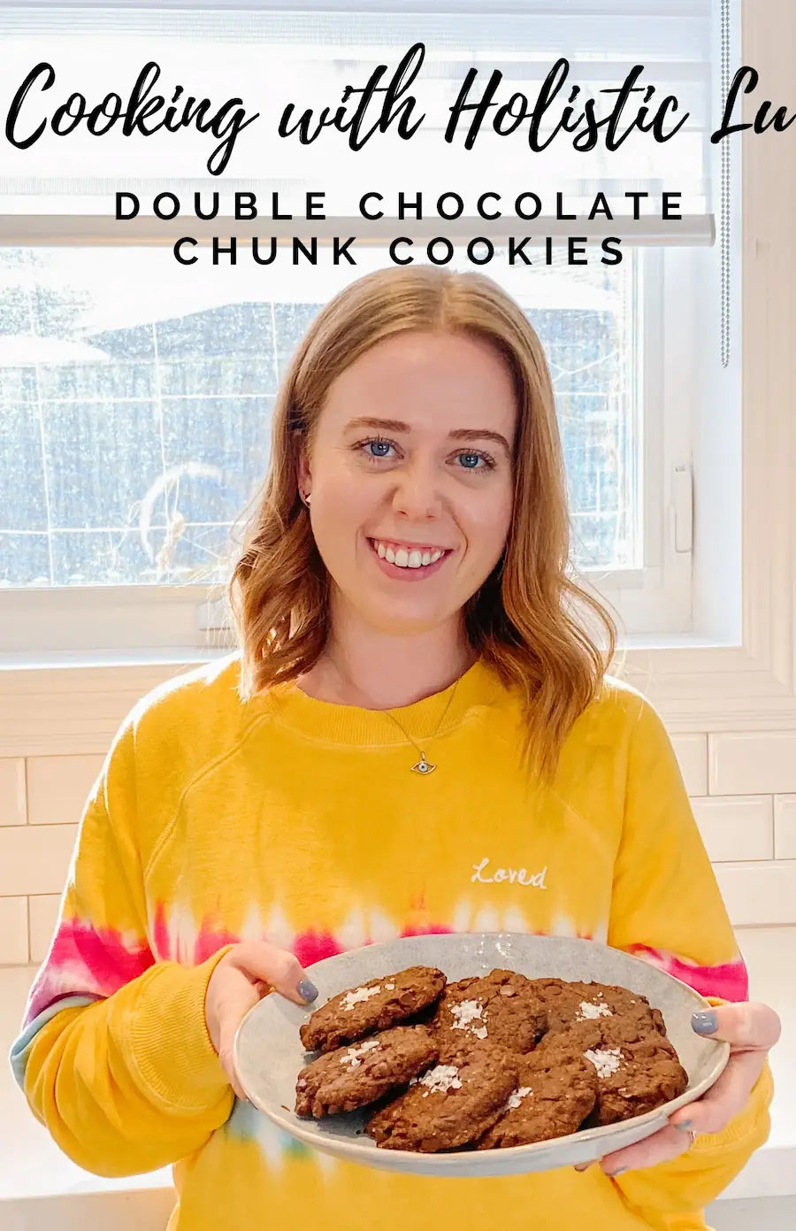 Lyndsay Reddick from Holistic Lu holding a plate of double chocolate chunk cookies in a bright kitchen.