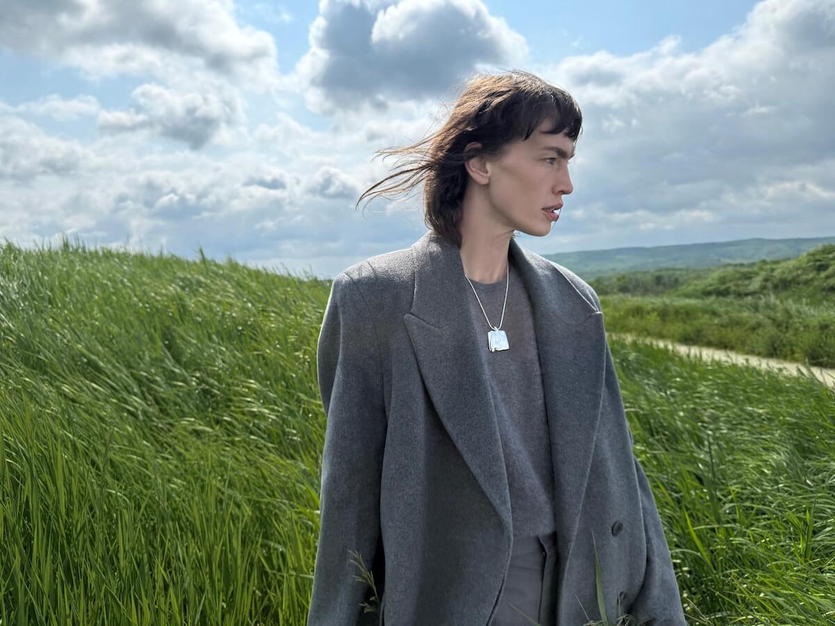 Woman wearing Jenny Bird silver pendant necklace and oversized blazer in a windswept green field — modern Canadian jewelry style.