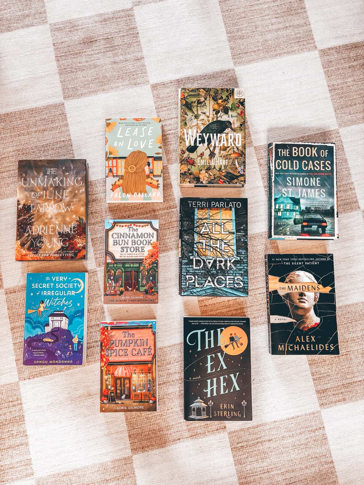 Flat lay of ten Lemonberry Book Club fall reading picks including romance, thrillers, and cozy autumn novels on a plaid blanket