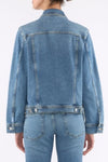 Back side of the 7 For All Mankind ADI Trucker Jacket in medium indigo wash worn by a person on a white background