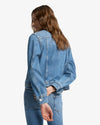 Person wearing a 7 For All Mankind ADI Trucker Jacket in medium indigo wash and jeans on a white background