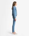 Woman wearing a 7 For All Mankind ADI Trucker Jacket in medium indigo wash and jeans on a white background