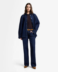 Person wearing a navy blue denim jacket and pants on a white background