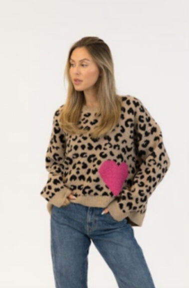 Woman in leopard print sweater with pink heart detail and blue jeans, white studio background