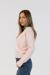 Woman wearing a light pink cardigan with pearl embellishments on a white background