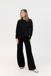 Woman wearing a black polka dot sweater and black pants on a white background
