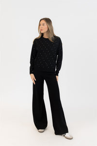 Woman wearing a black polka dot sweater and black pants on a white background