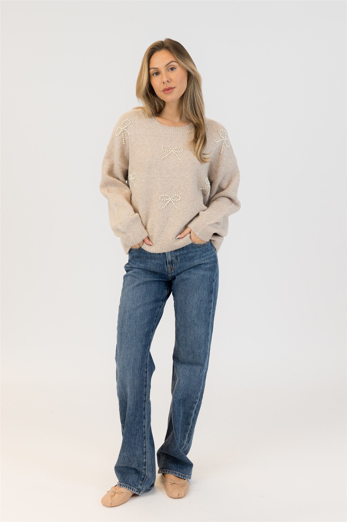 Model wearing Lyla & Luxe BOWS-F25 eco crewneck sweater with pearl bows in beige, standing studio view – Lemonberry