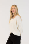 Woman wearing a white sweater and black pants against a plain background