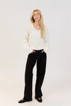 Woman wearing a white sweater and black pants on a white background