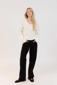 Woman wearing a white sweater and black pants on a white background