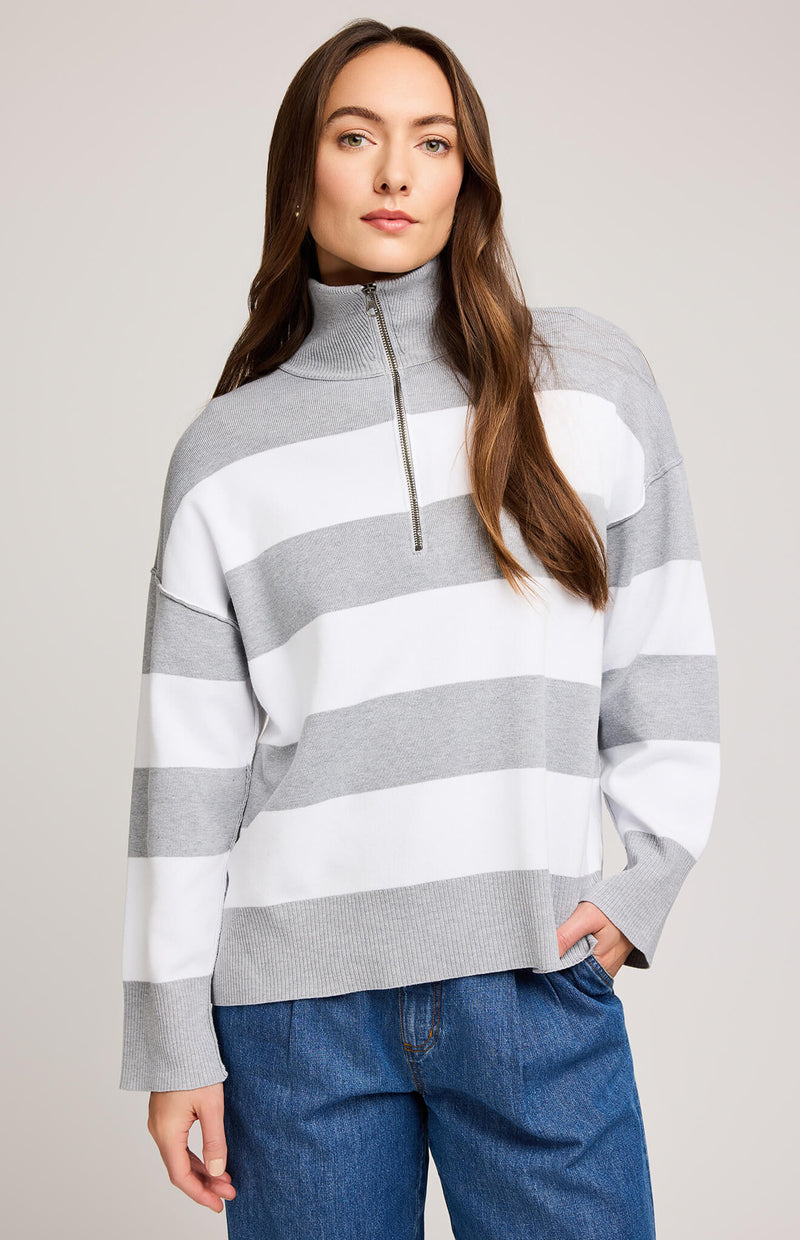 Woman wearing a gray and white striped sweater with a high collar on a plain background