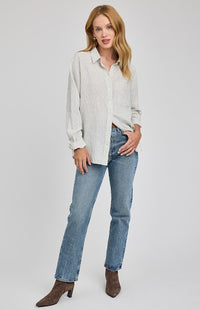 Woman wearing a white striped button-down shirt by Gentle Fawn and jeans on a plain background