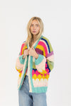 Full-body image of woman in rainbow-striped Haven Cardigan by Lyla & Luxe, styled with light-wash jeans, photographed at Lemonberry in Aurora