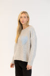 Model wearing grey sweater with pastel blue heart, angled side view