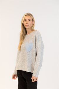 Model wearing grey sweater with pastel blue heart, angled side view
