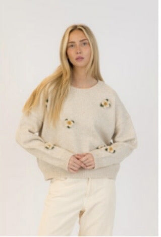 Model wearing oat knit sweater with embroidered flowers and cream pants