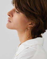 Woman wearing gold hoop earrings against a light background
