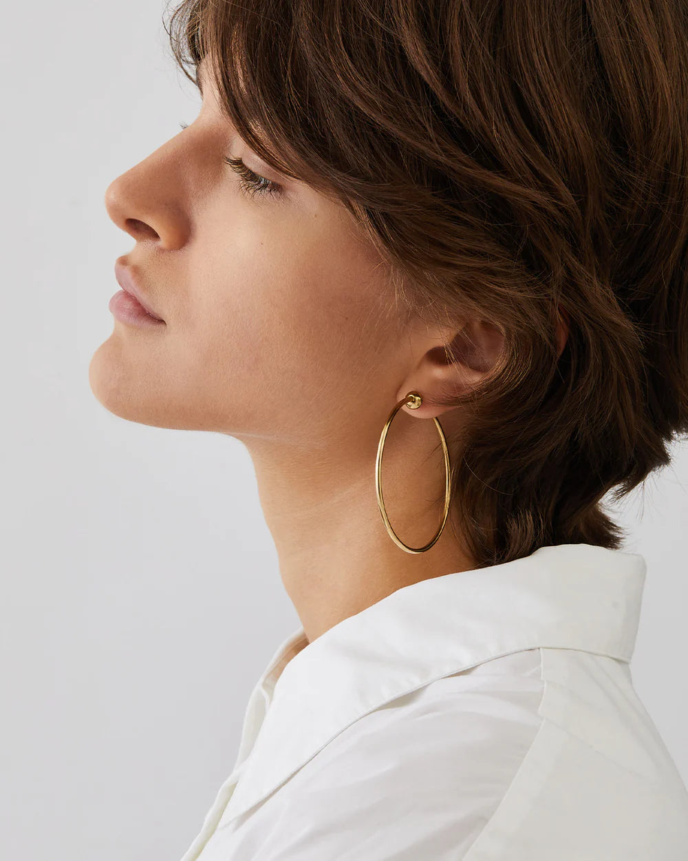 Woman wearing gold hoop earrings against a light background