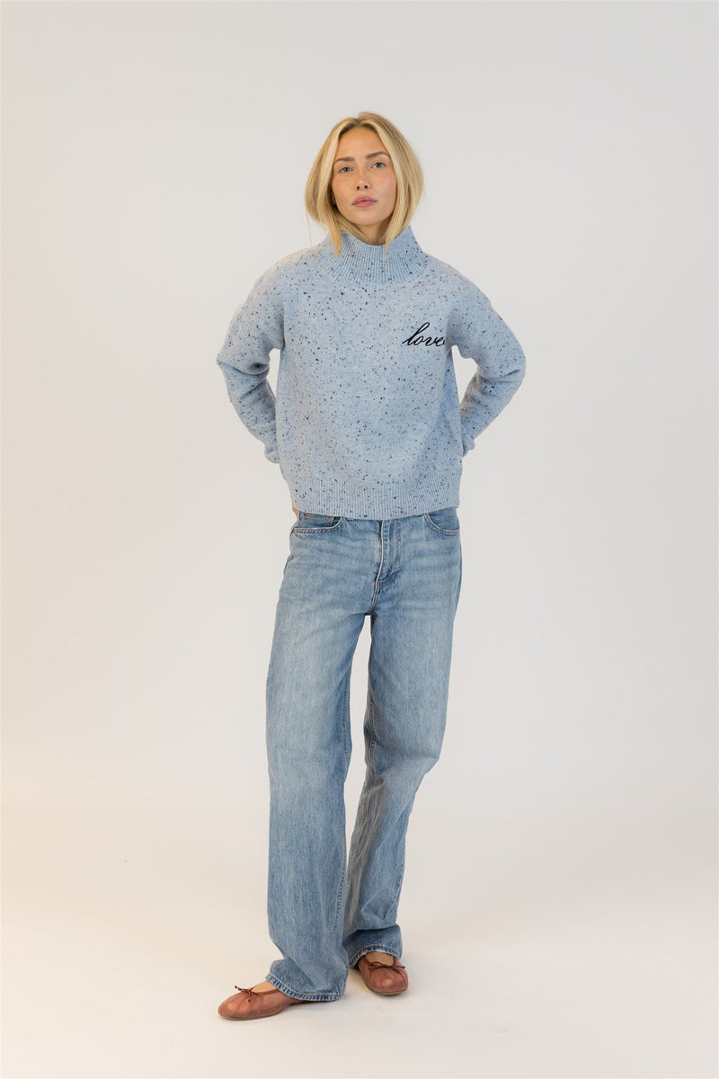 Person wearing a light blue turtleneck sweater by Lyla & Luxe with jeans on a white background