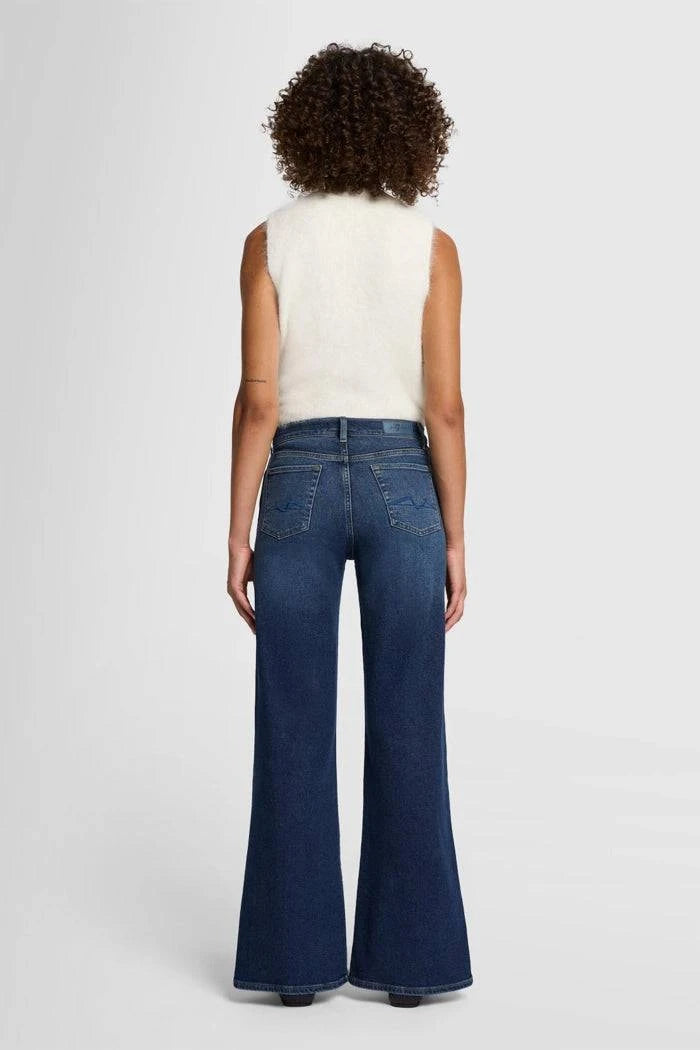 Model wearing 7 For All Mankind Lotta High-Waist Flare Jeans in Dark Blue, back view.