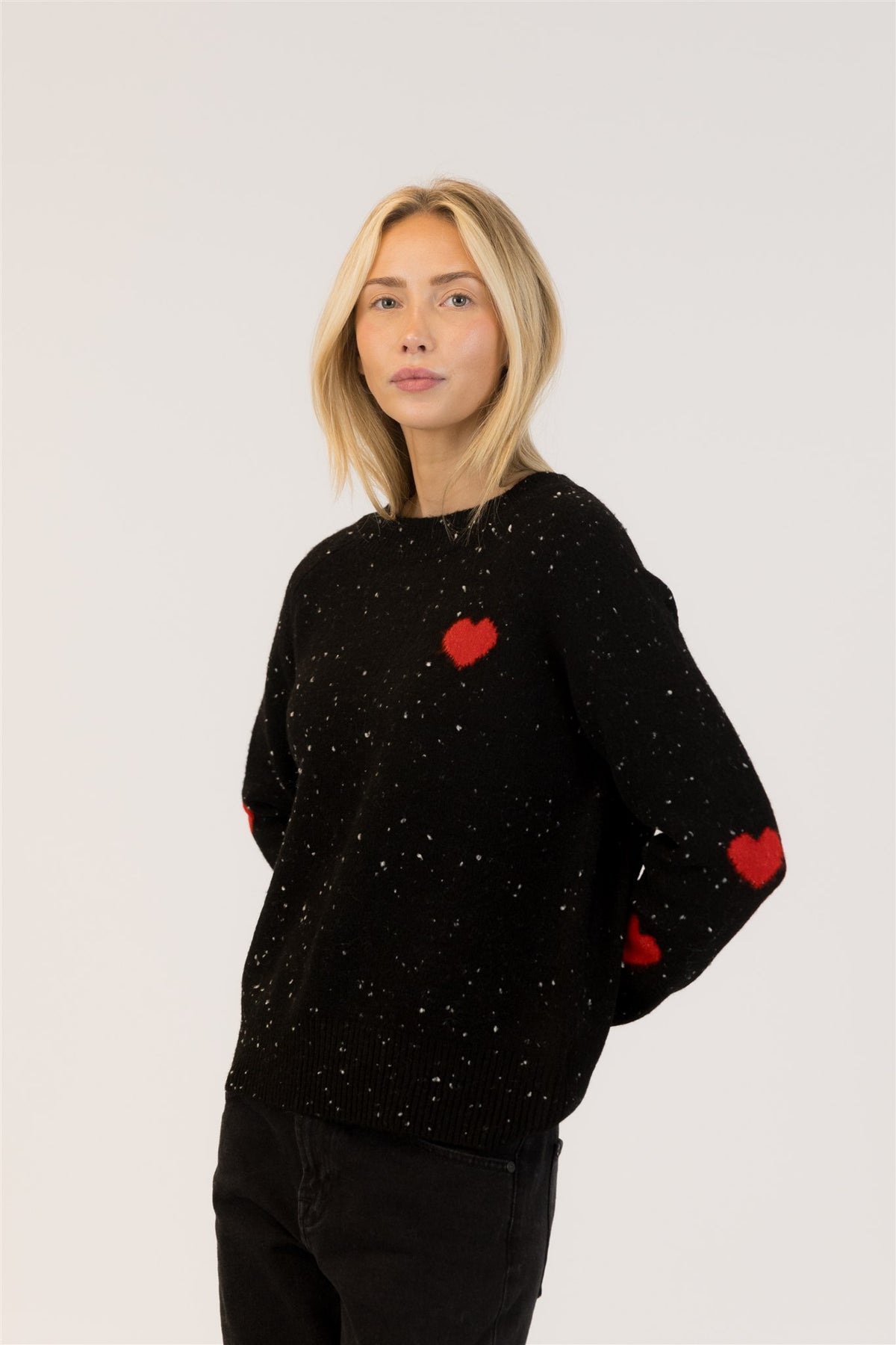 Angled view of black fleck crewneck sweater with red heart chest patch
