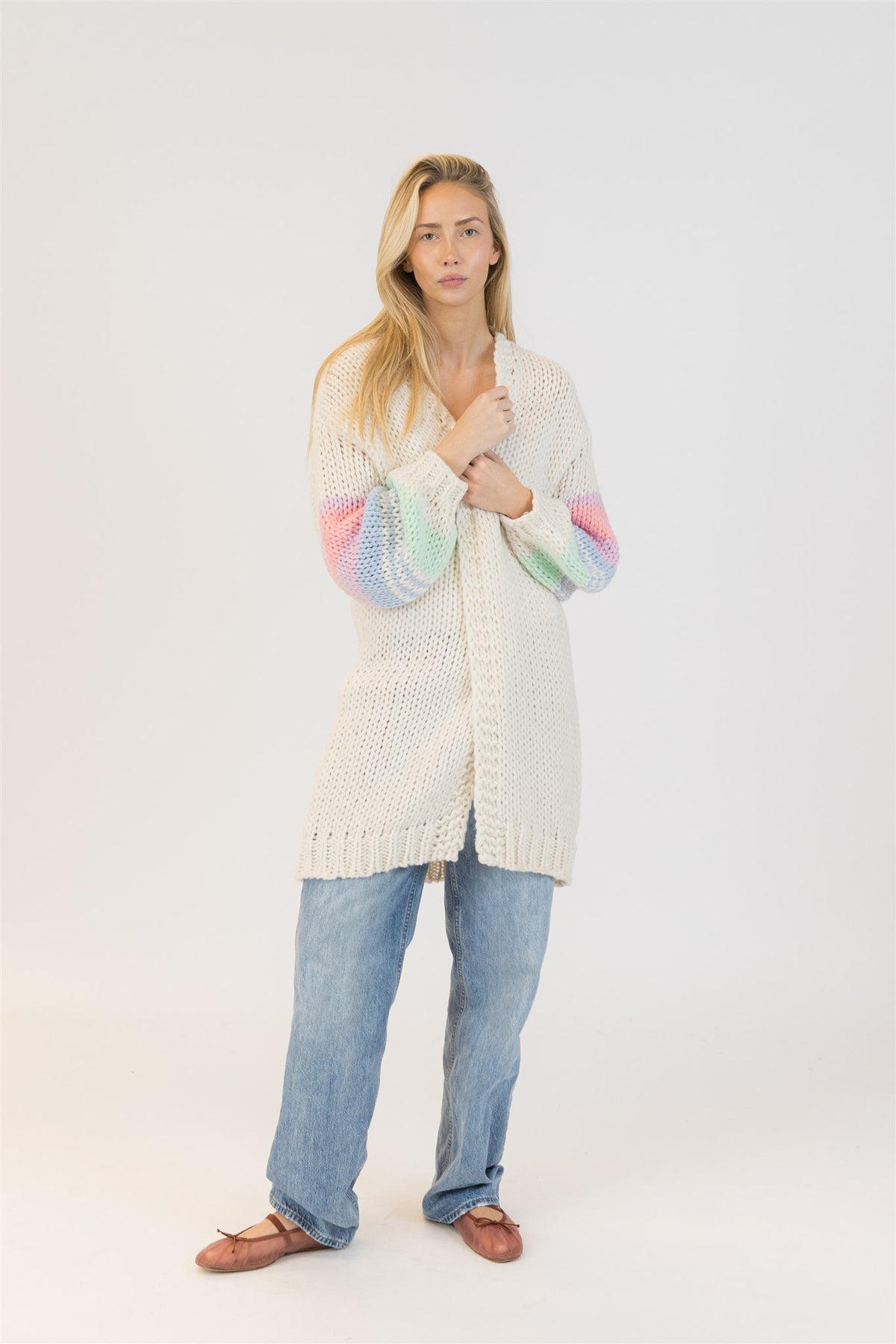 Model wearing Lyla + Luxe Shiloh cardigan, standing front view with hands at chest, showcasing rainbow sleeves – photographed in studio for Lemonberry in Aurora