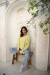 A yellow waffle-knit sweater paired with denim jeans, with the model sitting on a bench. Lemonberry, Aurora, ON