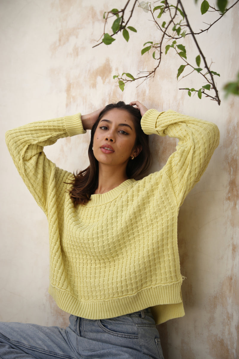 A yellow waffle-knit sweater by Echo Verde, close up, paired with denim jeans.
