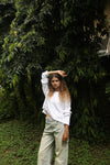 A white colored waffle-knit sweater paired with linen pants, with model raising one arm, displaying the relaxed drape.