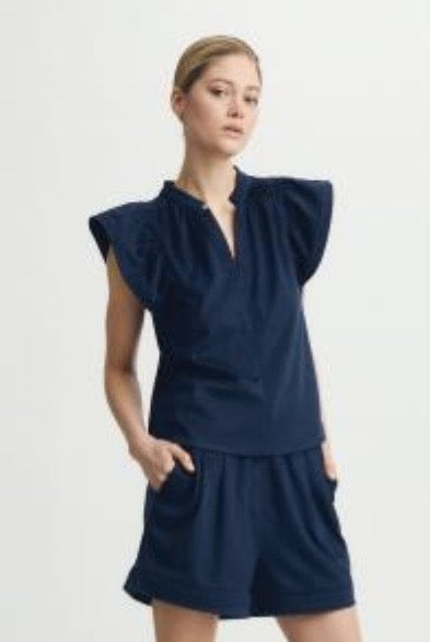 Woman wearing a navy blue Venora top by Melissa Nepton, with ruffled sleeves on a light background