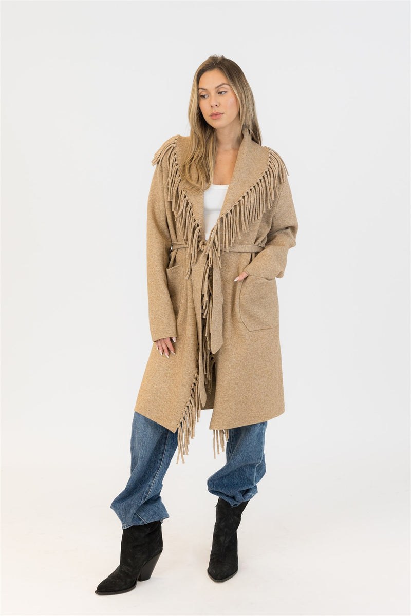 Woman wearing Lyla + Luxe Ziggy fringe coat in camel beige with black boots, hands in pockets – front view
