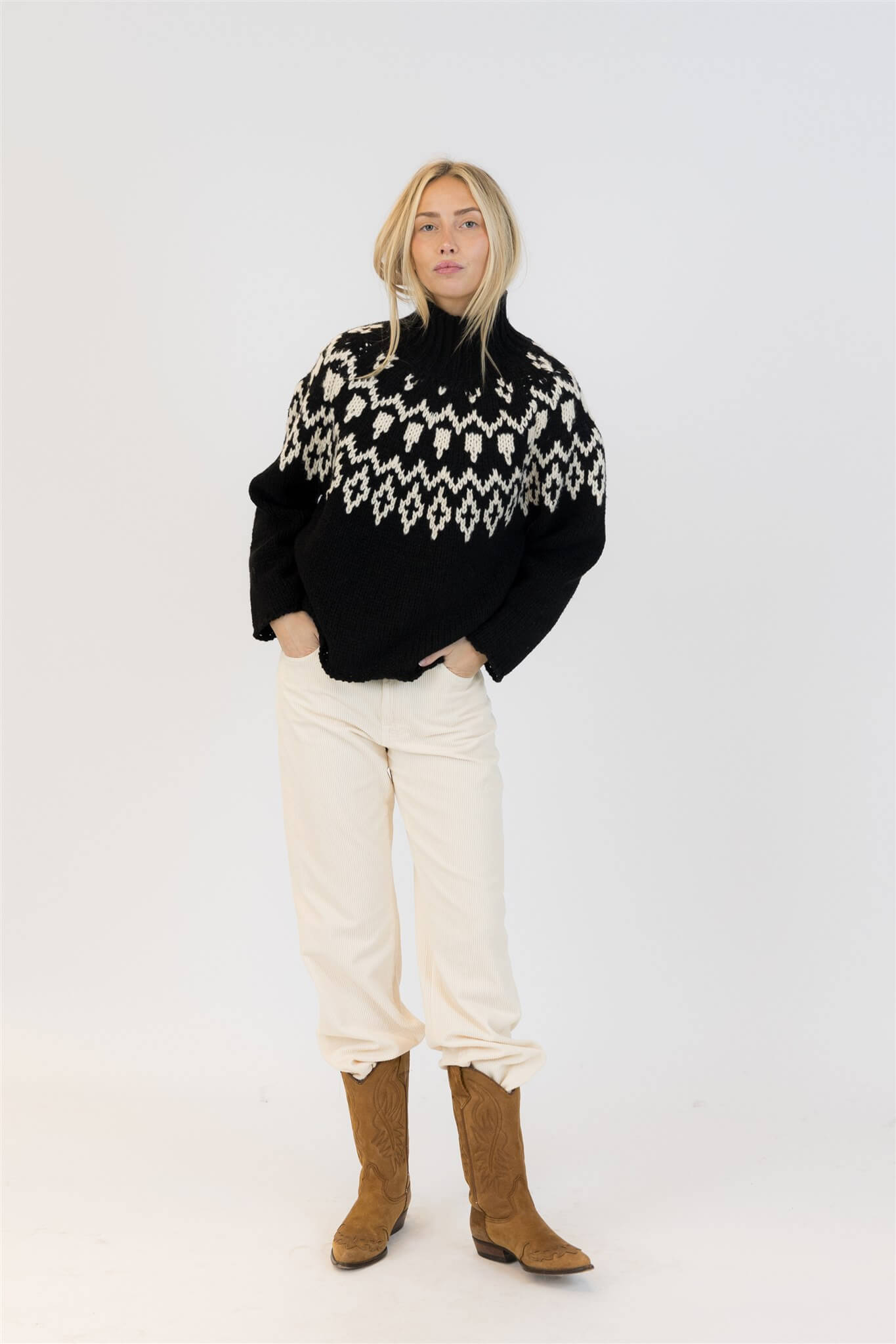 Black and white Fair Isle sweater styled with tan cowboy boots and cream pants for a chic winter vibe.