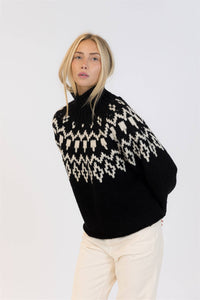 Model wearing Lyla & Luxe black and white Fair Isle sweater with high neck and cream corduroy pants.