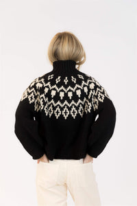 Back view of Lyla & Luxe Aggie Fair Isle turtleneck sweater in black and white, styled with cream pants.

