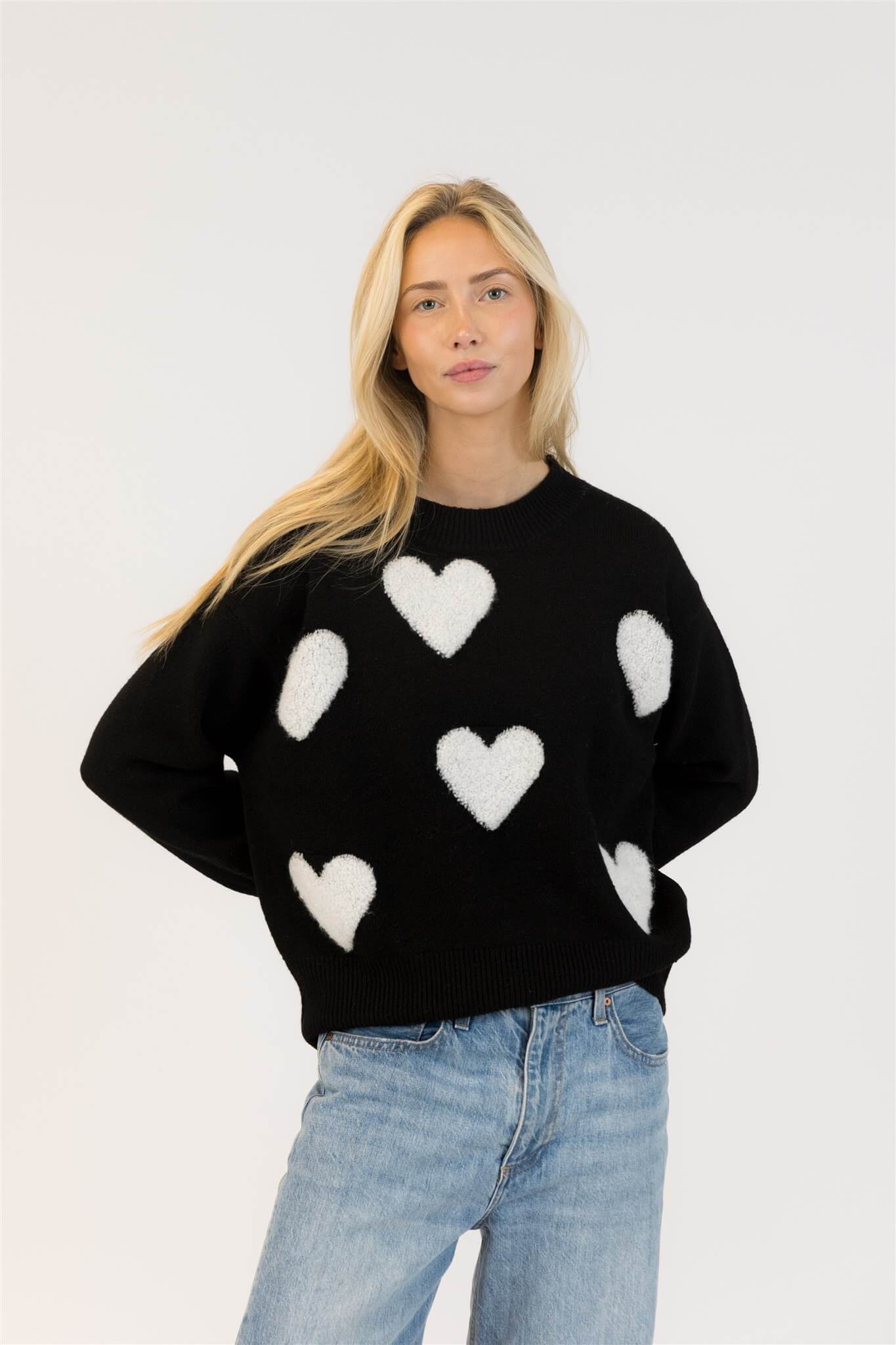 Front view of Lyla & Luxe Ajax Sherpa Sweater in black with white heart appliqués, styled with light blue jeans

