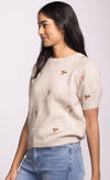 Side view of Alva Sweater by Pink Martini, short sleeve neutral knit with whimsical floral embroidery.