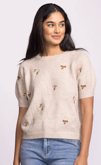 Closeup of Alva Sweater’s lightweight beige knit with tiny embroidered flowers, styled with denim.