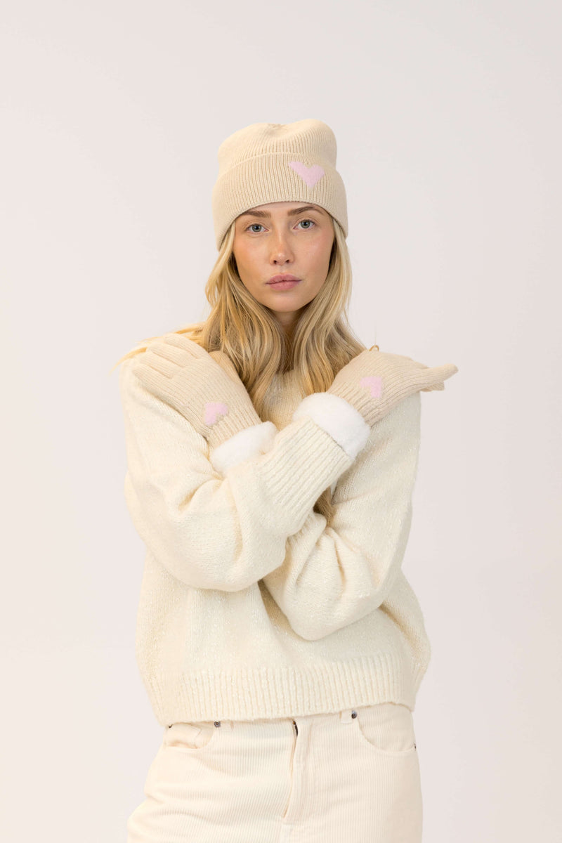 Woman wearing a cream-colored outfit with heart details on a light pink background