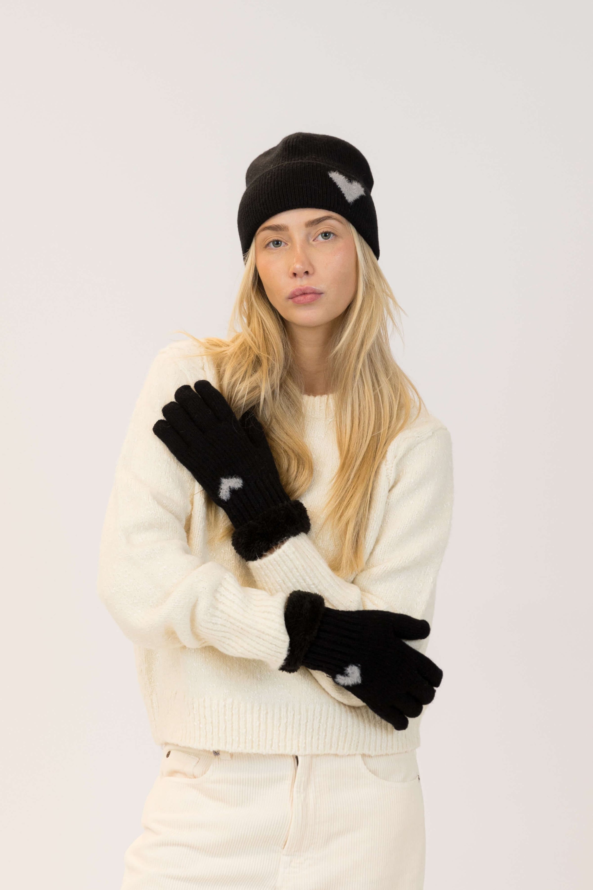 Woman wearing a black beanie, white sweater, and black gloves on a light gray background