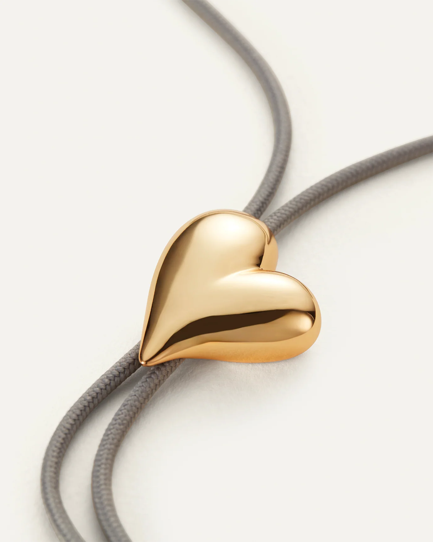 Gold heart-shaped pendant on a gray cord against a white background