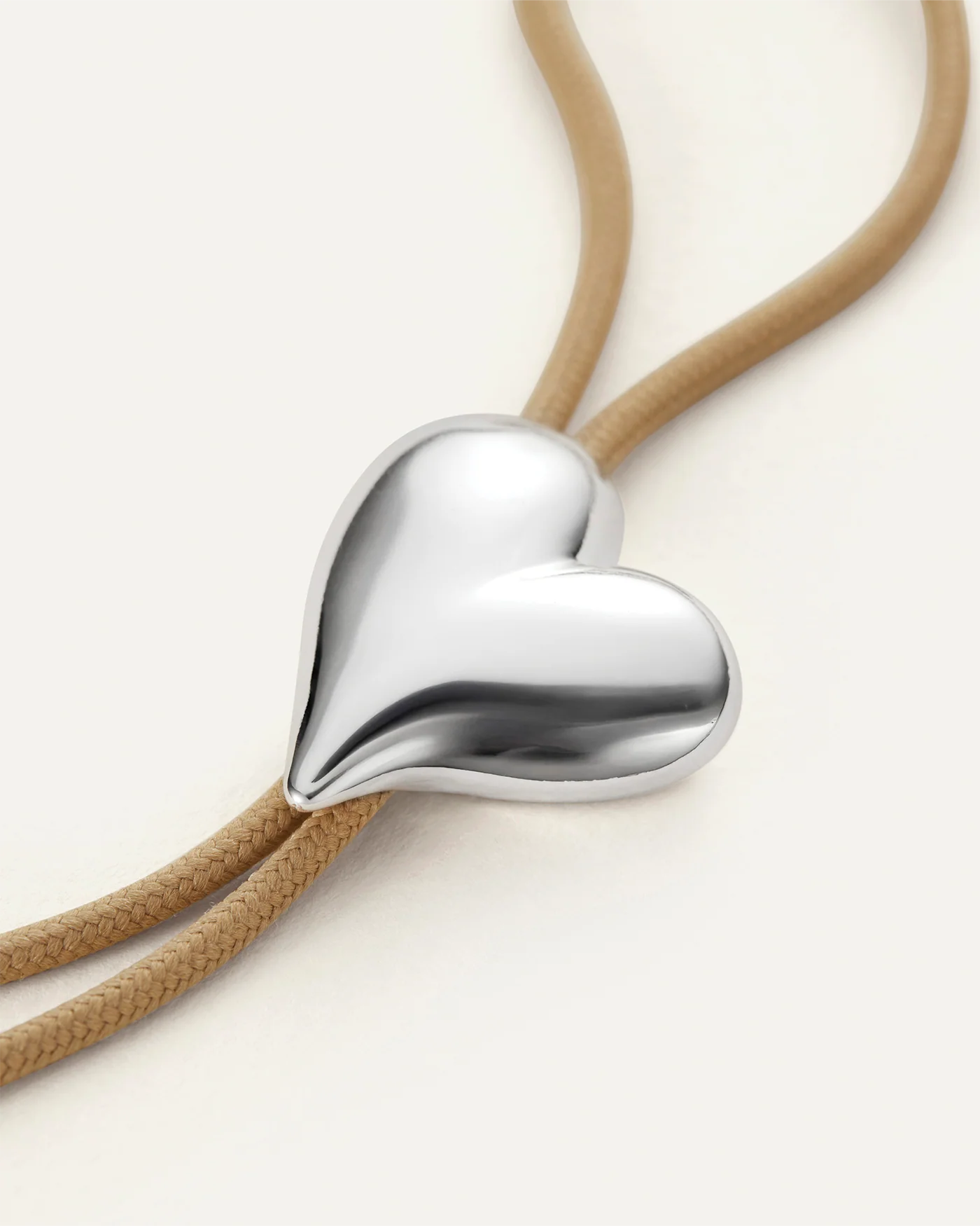 Heart-shaped silver pendant on a beige cord against a white background