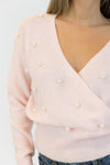Light pink sweater with pearl embellishments on a plain background