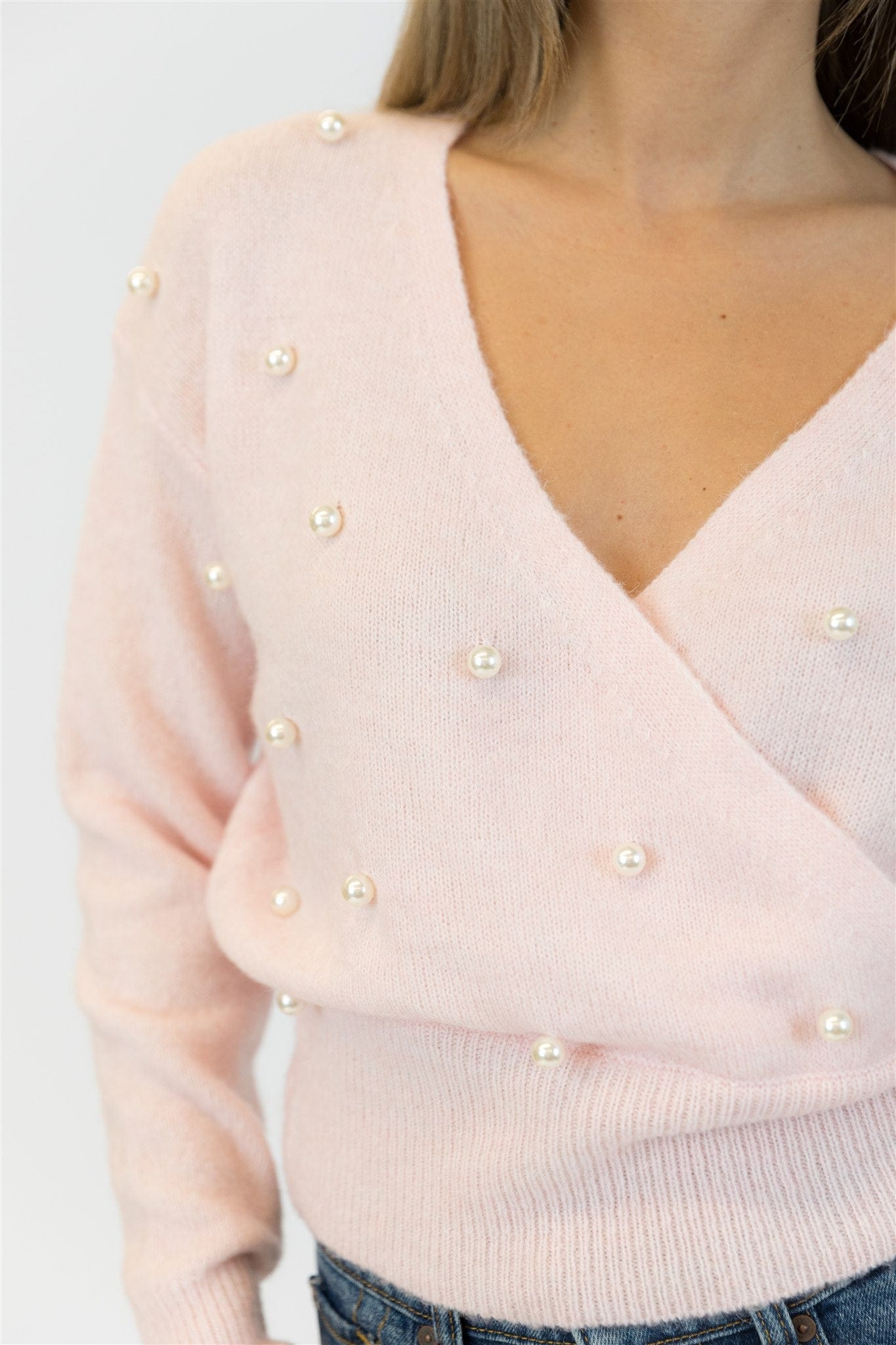 Light pink sweater with pearl embellishments on a plain background