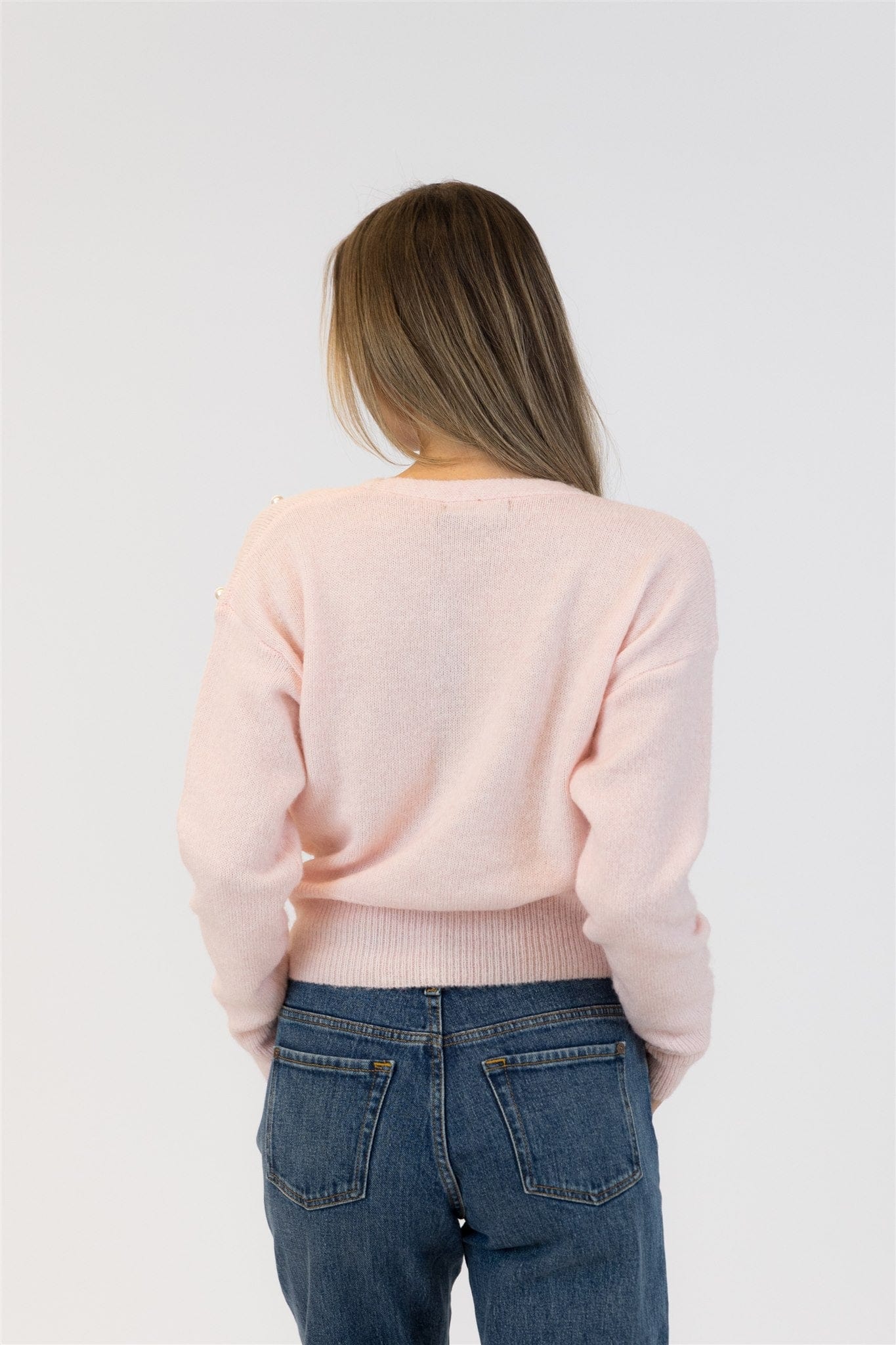Person wearing a light pink sweater and blue jeans on a white background